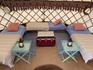 Inside a furnished yurt with three single beds, side tables, lanterns, and a central trunk.