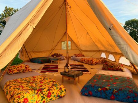 Inside a large canvas tent with four single beds and small side tables.