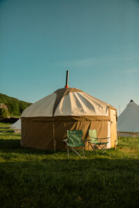 A yurt with two folding chairs on grass under a clear sky.