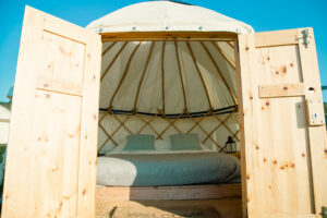 Open wooden doors frame a yurt interior with a bed and pillows.