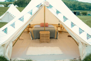A decorated bell tent with a bed, bedside tables, and a rug inside.
