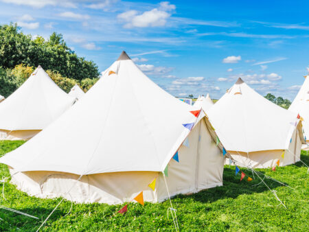 White bell tents on grass under a blue sky.
