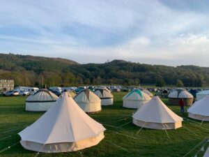 Canvas tents set up on a grassy field with hills in the background.