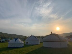 Yurts on a grassy field at sunset with hills in the background.
