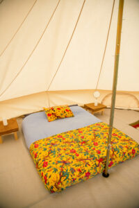 A furnished bell tent with a bed, bedside tables, and patterned bedding.