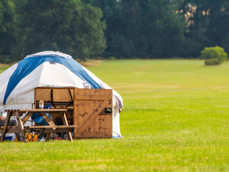 A small yurt with a wooden table and chairs on a grassy field.