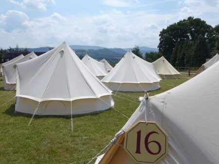 Several white bell tents pitched on grass with hills in the background.