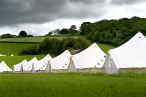 A row of white tents set up in a grassy field with hills and trees under dark clouds.